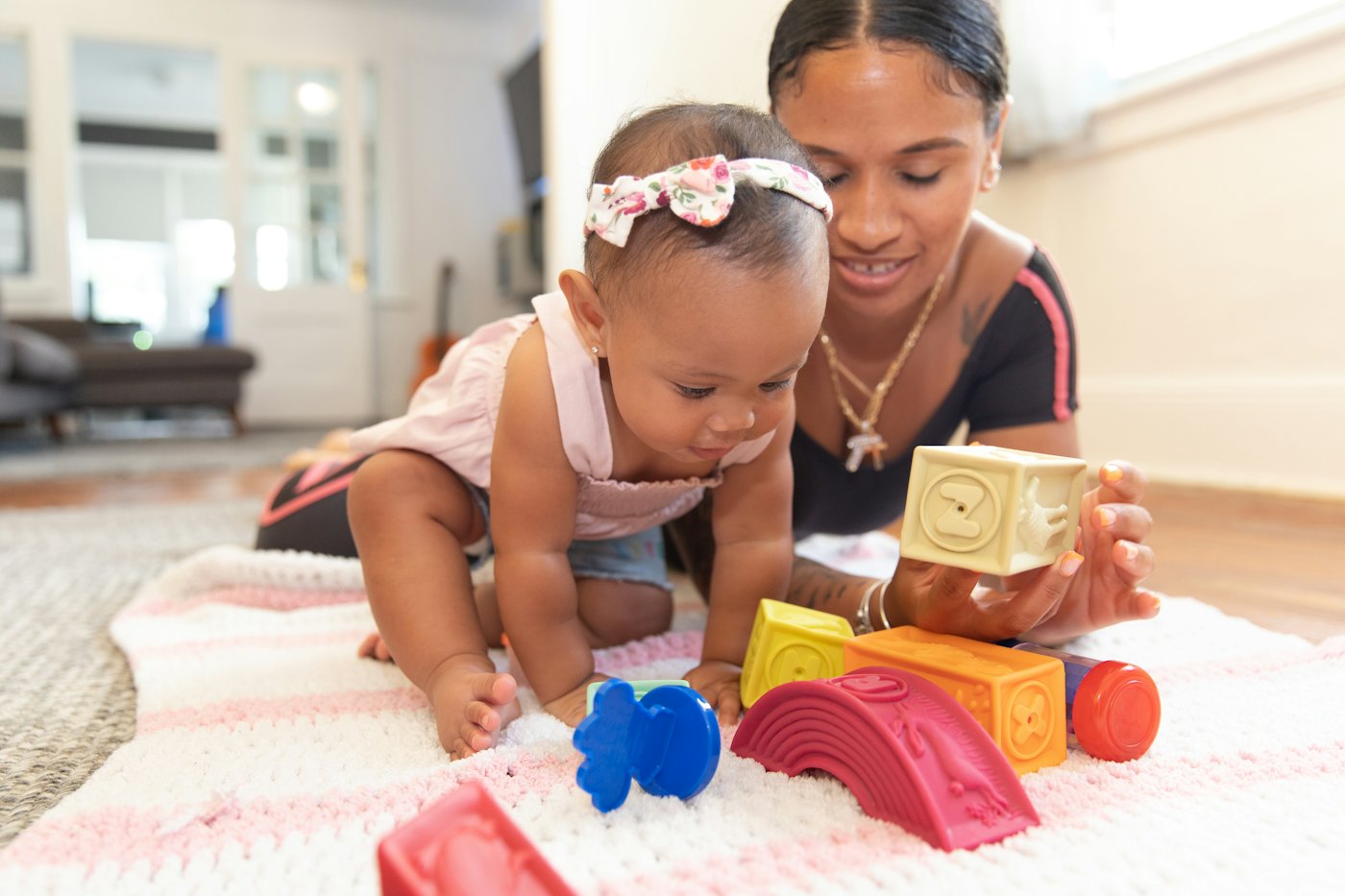 Cuidadora sorridente brincando com um bebê sobre um tapete, com blocos coloridos