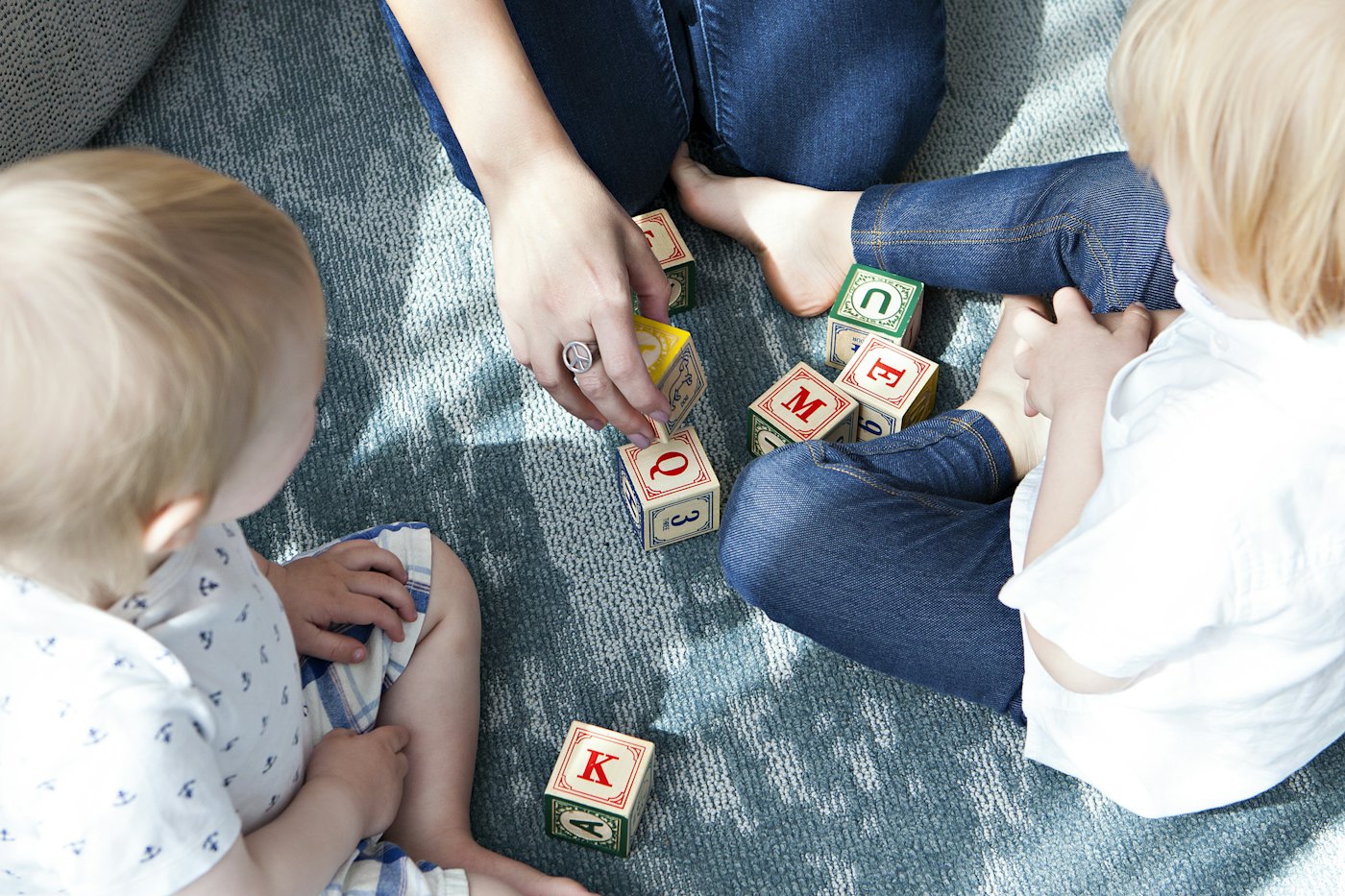 Adulta brincando no chão com duas crianças pequenas, montando cubos de letras